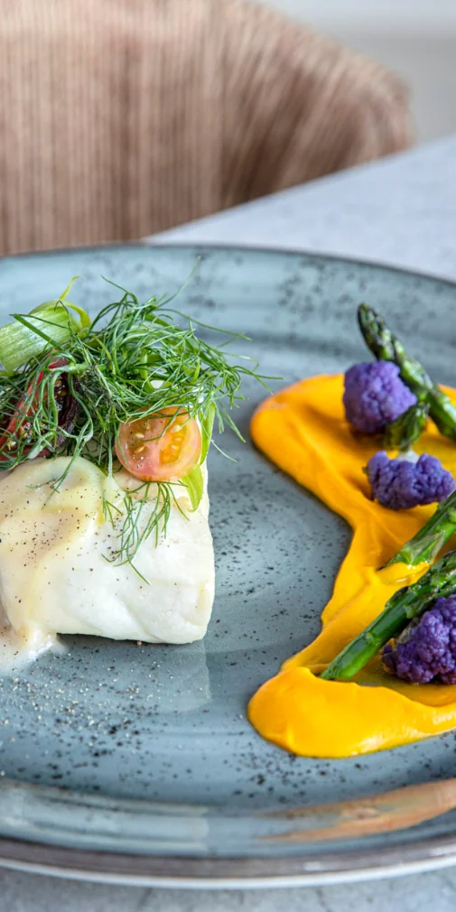 Plated fish dish with vibrant sauce and seasonal vegetables.